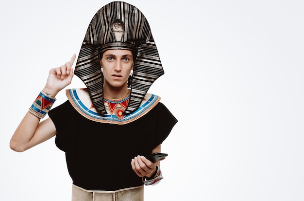 Uomo in costume egiziano antico che tiene smartphone puntato con il dito indice su bianco