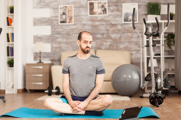 Uomo in forma che guarda la lezione di yoga online durante il blocco covid-19.