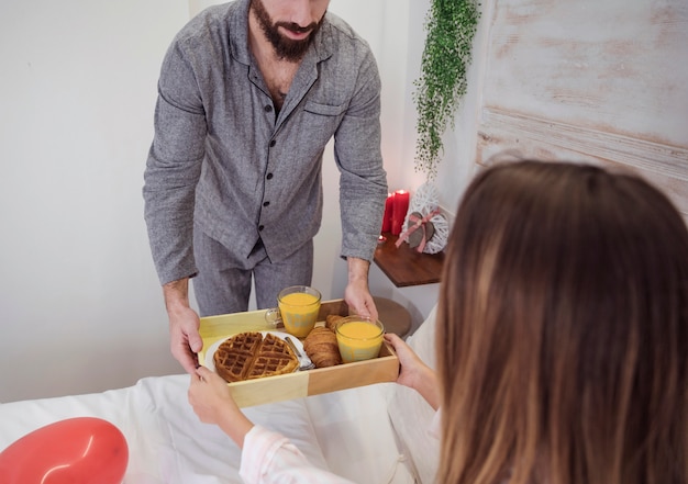 Uomo in grigio dando vassoio con colazione romantica alla donna