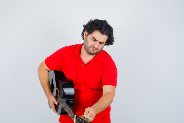 uomo in maglietta rossa, suonare la chitarra e guardare concentrato