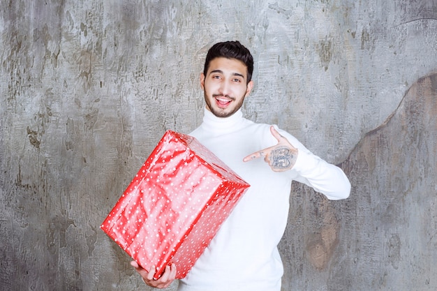 Uomo in maglione bianco che tiene una confezione regalo rossa con puntini bianchi su di esso.