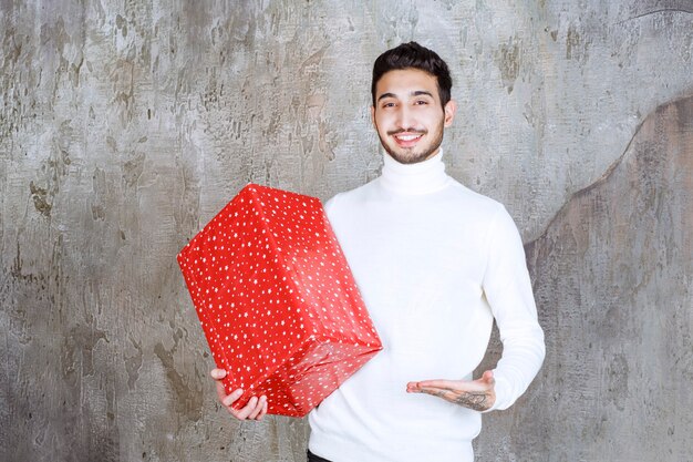 Uomo in maglione bianco che tiene una confezione regalo rossa con puntini bianchi su di esso.