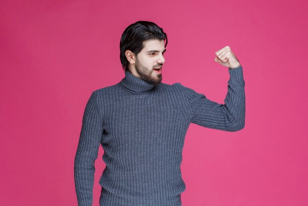 Uomo in maglione grigio che dimostra i suoi muscoli del braccio.