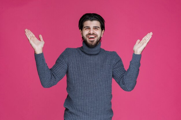 Uomo in maglione grigio che presenta o saluta qualcuno con grande energia ed entusiasmo.