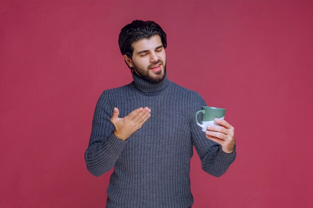 Uomo in maglione grigio che tiene una tazza di caffè e lo indica.