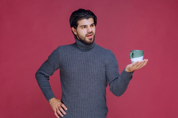 Uomo in maglione grigio che tiene una tazza di caffè in mano.
