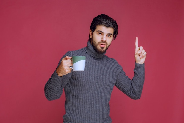 Uomo in maglione grigio che tiene una tazza e chiede attenzione.