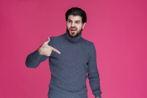 Uomo in maglione grigio per indicare qualcosa o presentare qualcuno usando il dito puntato.