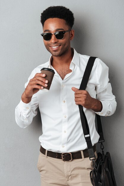 Uomo in occhiali da sole che indossa una borsa e che tiene la tazza di caffè