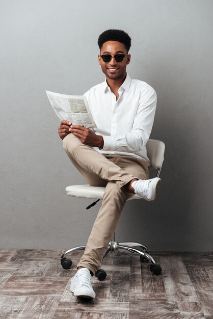 Uomo in occhiali da sole che tiene giornale mentre era seduto su una sedia