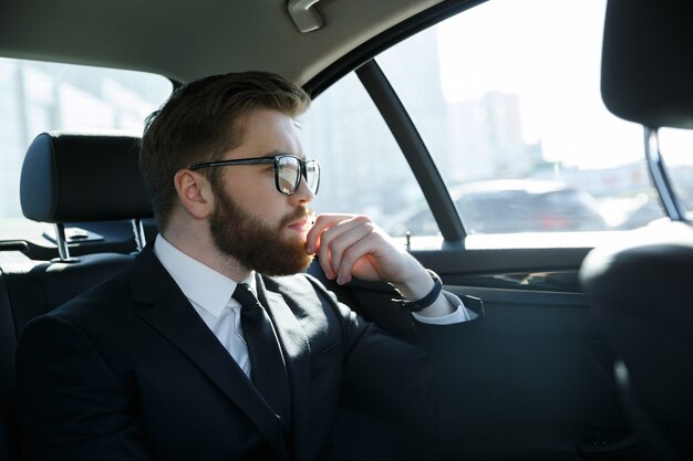 Uomo in occhiali seduto sul sedile posteriore della macchina