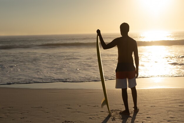 Uomo in piedi con la tavola da surf sulla spiaggia