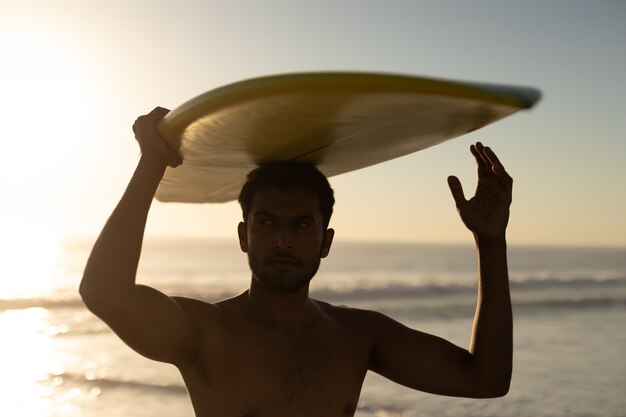 Uomo in piedi con la tavola da surf sulla spiaggia