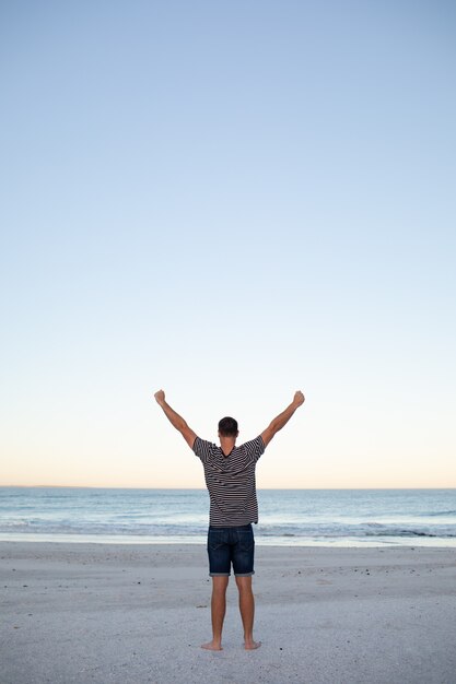 Uomo in piedi con le braccia in alto sulla spiaggia