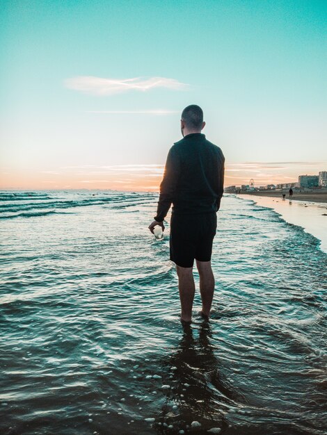 Uomo in piedi in acqua di mare con un bicchiere in mano