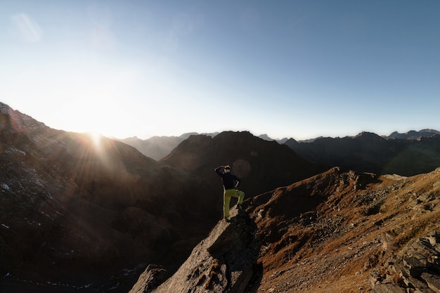 Uomo in piedi sulla roccia in cima alla montagna di fronte al sole