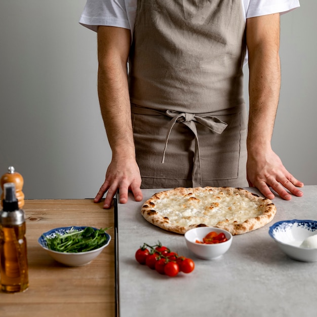 Uomo in piedi vicino a pasta per pizza al forno con ingredienti