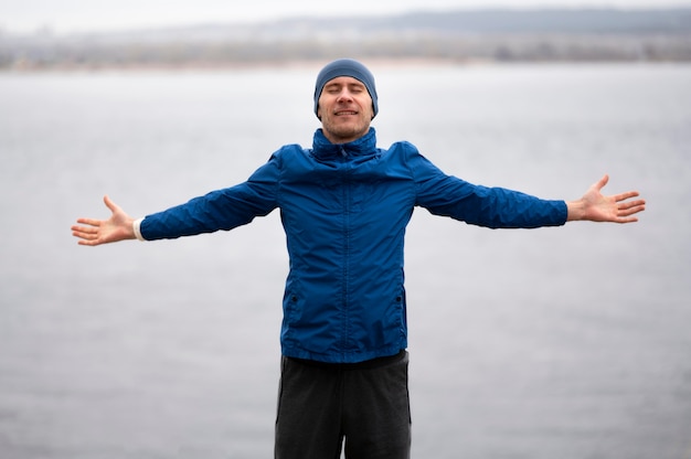 Uomo in piedi vicino al lago con le braccia aperte