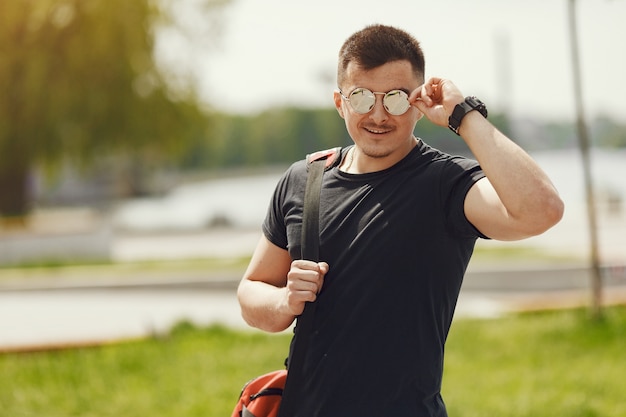 Uomo in piedi vicino all'acqua. Ragazzo in abiti sportivi. Maschio in un parco estivo con zaino