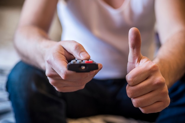 Uomo in possesso di un telecomando a cavo tv, guardando la tv. Stile di vita, intrattenimento, giovani. Moda, design e concetto di interni. Gli uomini con il telecomando mostrano il pollice in su