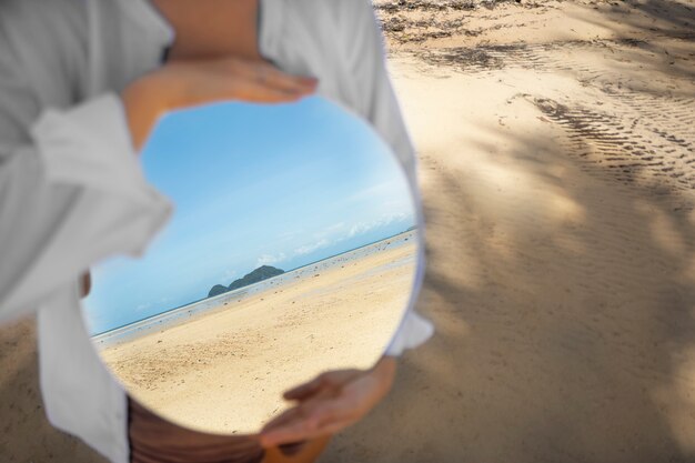 Uomo in spiaggia in posa con specchio riflettente rotondo