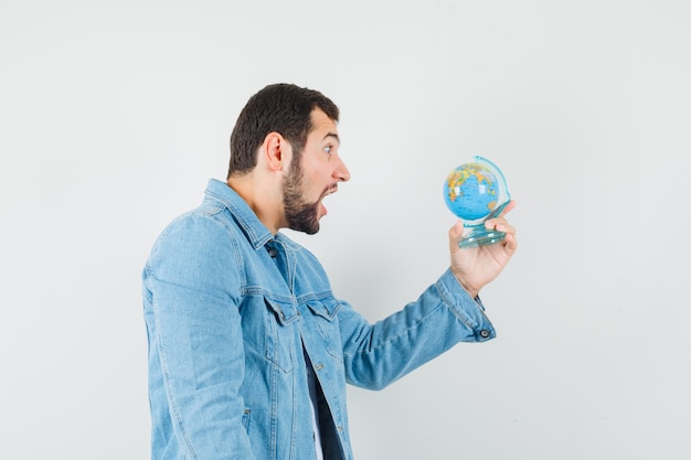 Uomo in stile retrò che guarda il mini globo in giacca, t-shirt e sembra turbato. vista frontale.