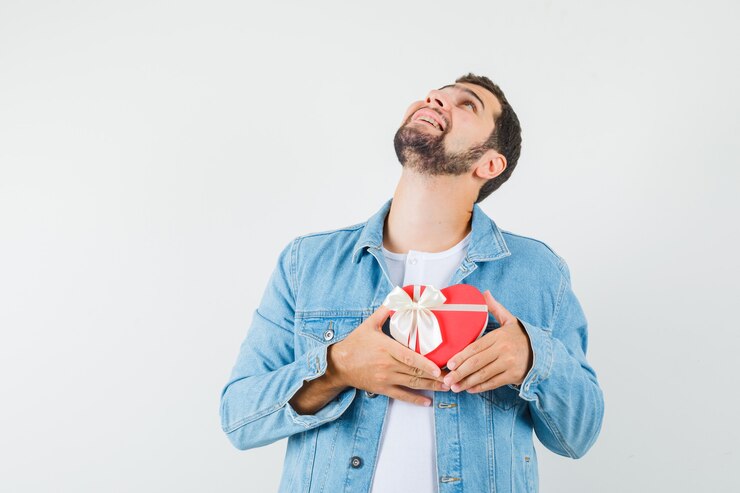 Foto gratuito uomo in stile retrò che mostra confezione regalo a forma di cuore in giacca, t-shirt e sembra un pio desiderio, vista frontale.