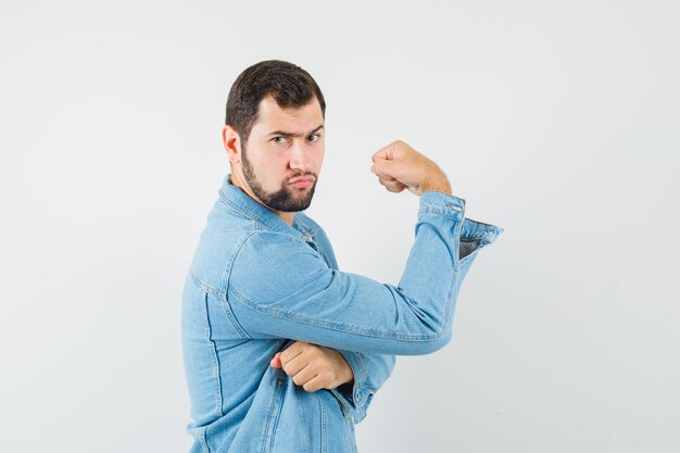 Uomo in stile retrò che mostra i muscoli delle braccia in giacca, t-shirt e sembra serio. vista frontale.