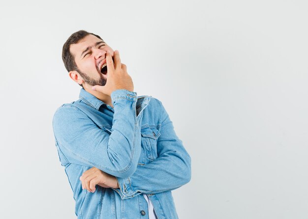 Uomo in stile retrò che sbadiglia con la mano sulla bocca in giacca, t-shirt e sembra assonnato. vista frontale.