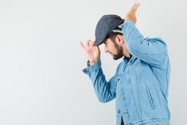 Uomo in stile retrò che si aggiusta il berretto in giacca, berretto e sembra concentrato, vista frontale. spazio per il testo