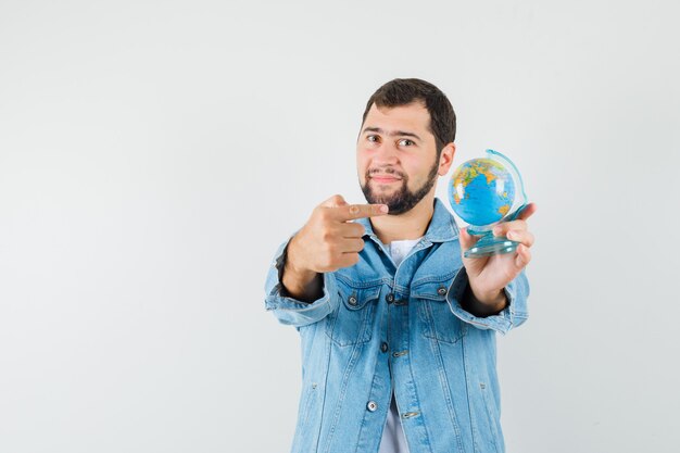 Uomo in stile retrò in giacca, t-shirt che punta al mini globo e che sembra soddisfatto, vista frontale.