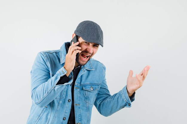 Uomo in stile retrò parla al telefono in giacca, berretto, camicia e sembra aggressivo. vista frontale.