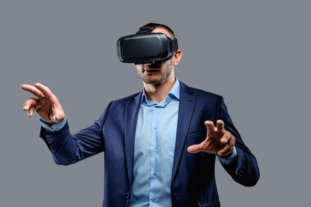 Uomo in tuta con occhiali per realtà virtuale in testa. Isolato su sfondo grigio.