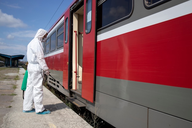 Uomo in tuta di protezione bianca che disinfetta e igienizza l'esterno del treno della metropolitana per fermare la diffusione del virus corona altamente contagioso