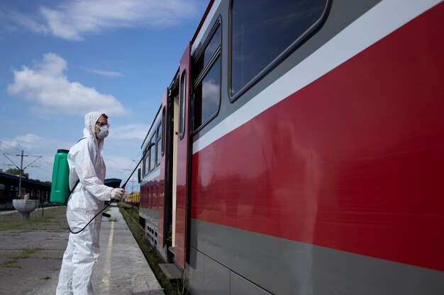 Uomo in tuta di protezione bianca che disinfetta e igienizza l'esterno del treno della metropolitana per fermare la diffusione del virus corona altamente contagioso