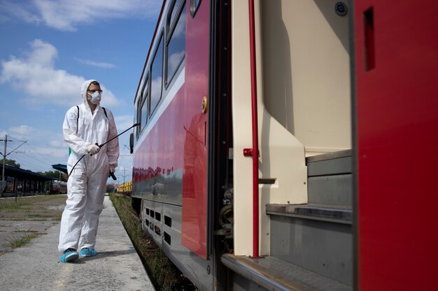 Uomo in tuta di protezione bianca che disinfetta e igienizza l'esterno del treno della metropolitana per fermare la diffusione del virus corona altamente contagioso