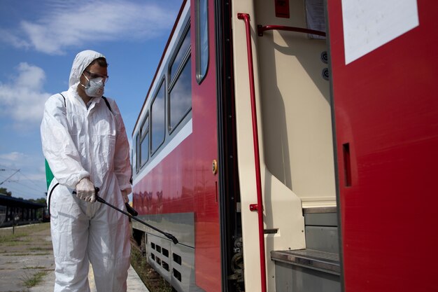 Uomo in tuta di protezione bianca che disinfetta e igienizza l'esterno del treno della metropolitana per fermare la diffusione del virus corona altamente contagioso
