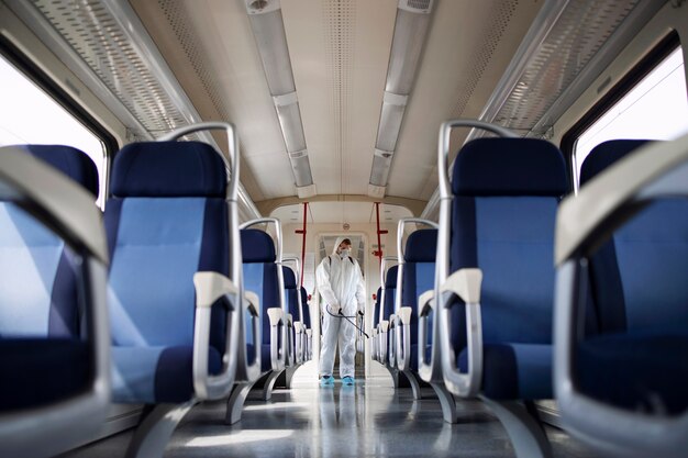 Uomo in tuta di protezione bianca che disinfetta e igienizza l'interno del treno della metropolitana per fermare la diffusione del virus corona altamente contagioso