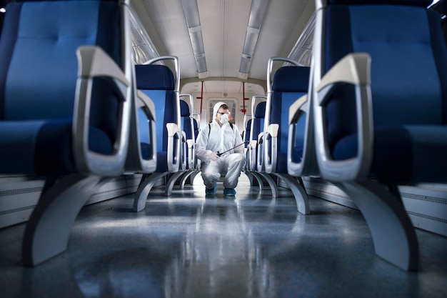 Uomo in tuta di protezione bianca che disinfetta e igienizza l'interno del treno della metropolitana per fermare la diffusione del virus corona altamente contagioso