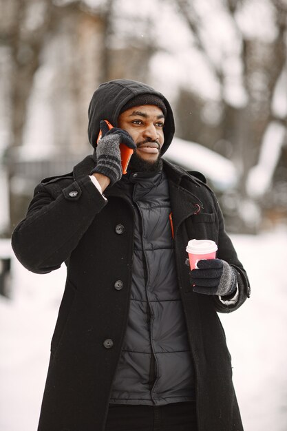 Uomo in una città invernale. Ragazzo con un cappotto nero. Uomo con caffè e telefono.