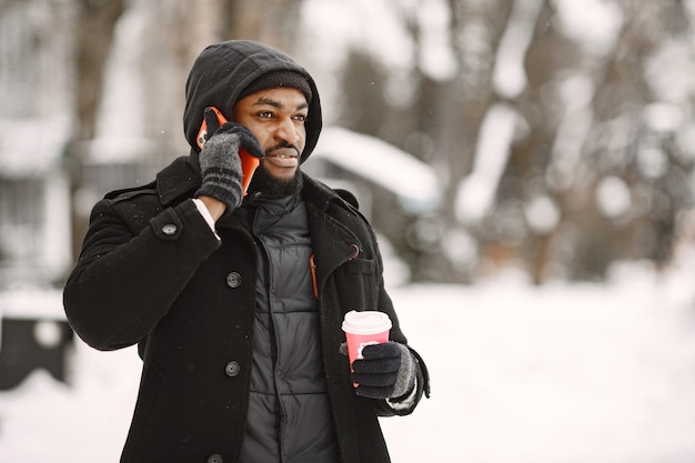 Uomo in una città invernale. Ragazzo con un cappotto nero. Uomo con caffè e telefono.