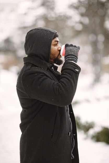 Uomo in una città invernale. Ragazzo con un cappotto nero. Uomo con il caffè.