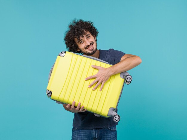 uomo in vacanza che tiene in mano una grande valigia gialla su blue