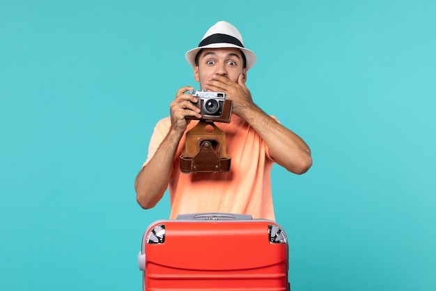 uomo in vacanza con la sua valigia rossa che scatta foto con la macchina fotografica su blue