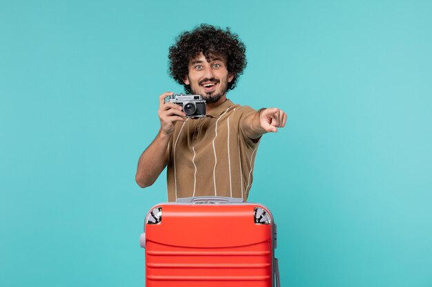 uomo in vacanza con valigia rossa che scatta foto con la fotocamera su azzurro