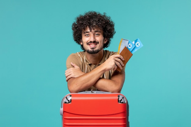 uomo in vacanza in possesso di biglietti e appoggiato alla sua borsa rossa su blue