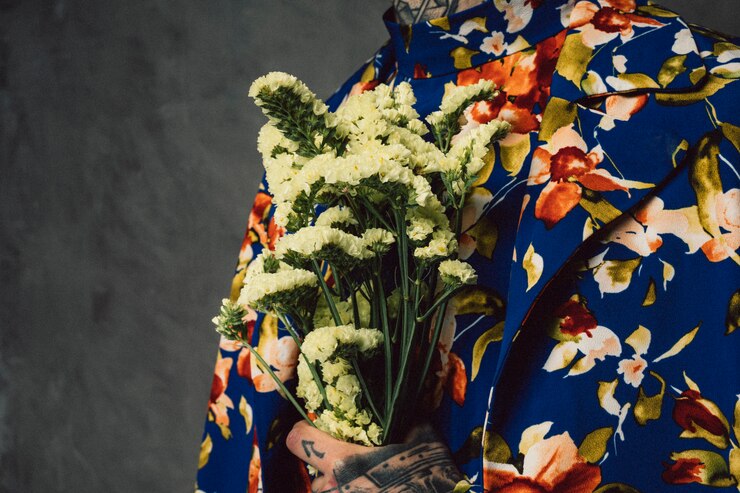 Foto gratuito uomo in vestito floreale che tiene il fiore giallo del limonium a disposizione