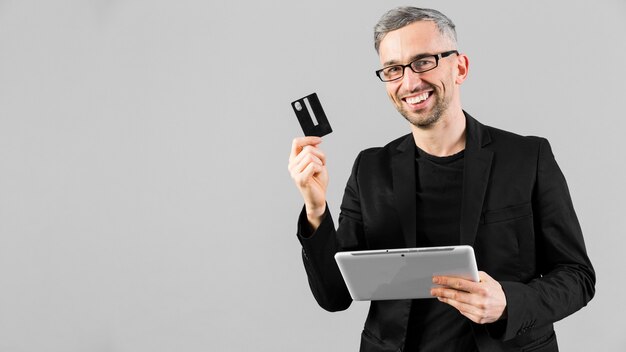 Uomo in vestito nero che mostra la carta di credito e la compressa