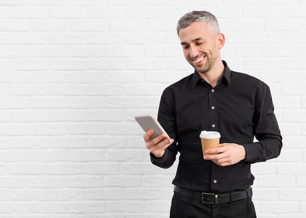 Uomo in vestito nero che tiene telefono e caffè