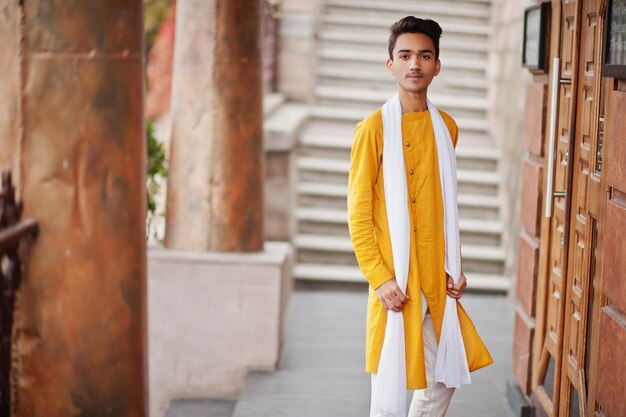 Uomo indiano alla moda in abiti tradizionali gialli con sciarpa bianca in posa all'aperto